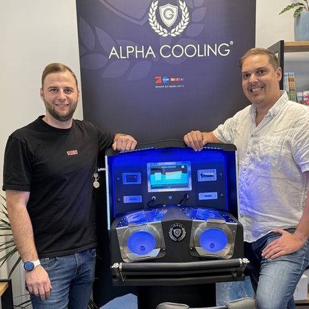 Zwei Männer stehen vor einer schwarzen und blauen Maschine mit dem Logo Alpha Cooling, lächeln und posieren für ein Foto.