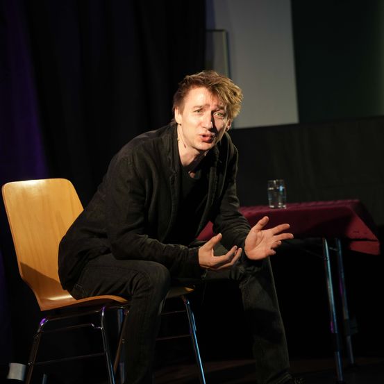 Bild enthält, Person, Solo Performance, People, Adult, Male, Man, Sitting, Crowd, Chair, Portrait