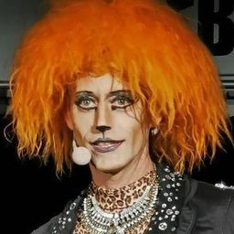 Eine Person mit orangefarbenen Haaren und Leopardenmuster-Kleidung, die vor einem Kleiderständer steht.