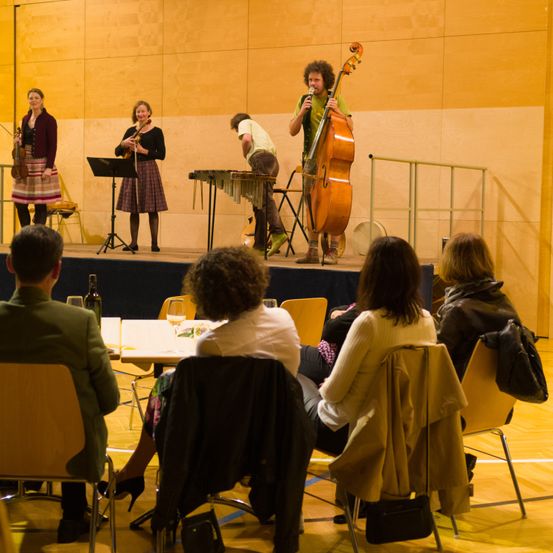 Eine kleine Gruppe von Musikern spielt auf der Bühne mit Cello, Violinen und einem Xylophon vor einem Publikum.