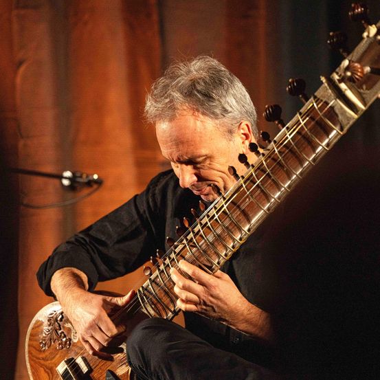 Ein Mann spielt ein Sitar, ein indisches Saiteninstrument, mit einem konzentrierten Ausdruck auf seinem Gesicht.