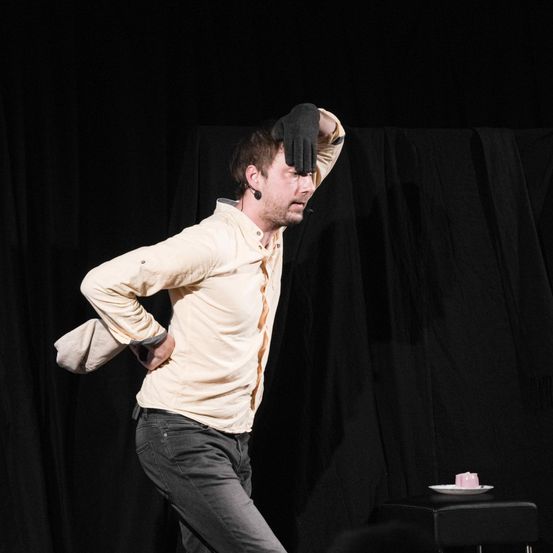 A man on stage with a glove on his head, performing a routine, has a microphone in his ear.