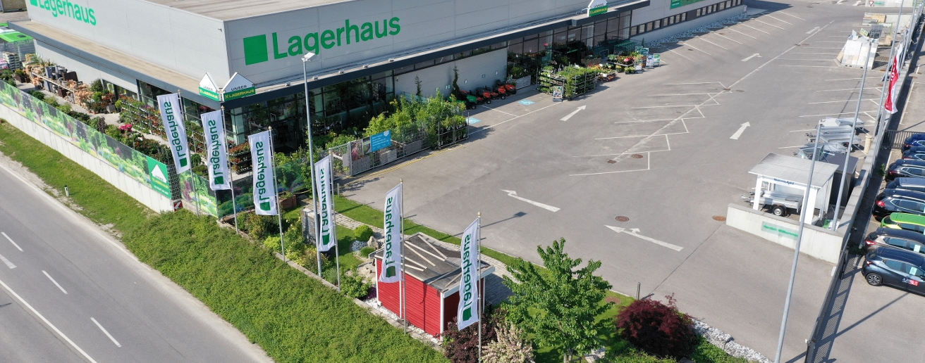 Eine Luftaufnahme des Lagerhaus-Geschäfts mit Bannern, einem roten Schuppen und einem Parkplatz.