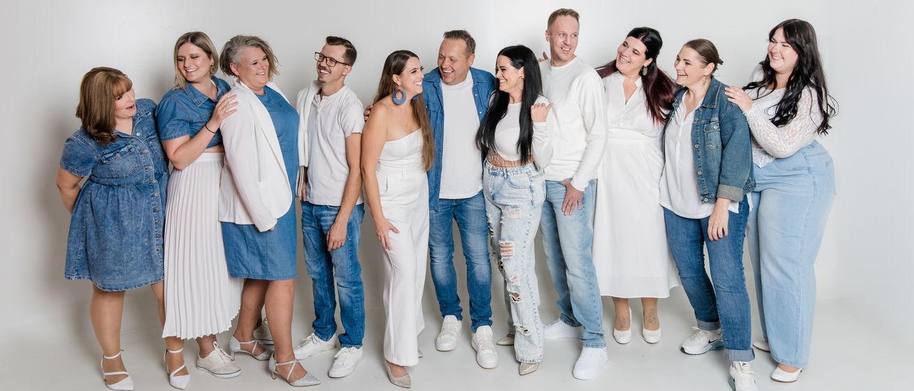 Eine Gruppe von Menschen, die in Weiß und Jeans gekleidet sind, lächeln und für ein Foto vor einem weißen Hintergrund posieren.
