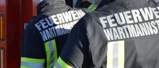 Zwei Feuerwehrleute in reflektierenden Uniformen, einer mit 'Feuerwehr' und 'Wartman' auf dem Rücken.