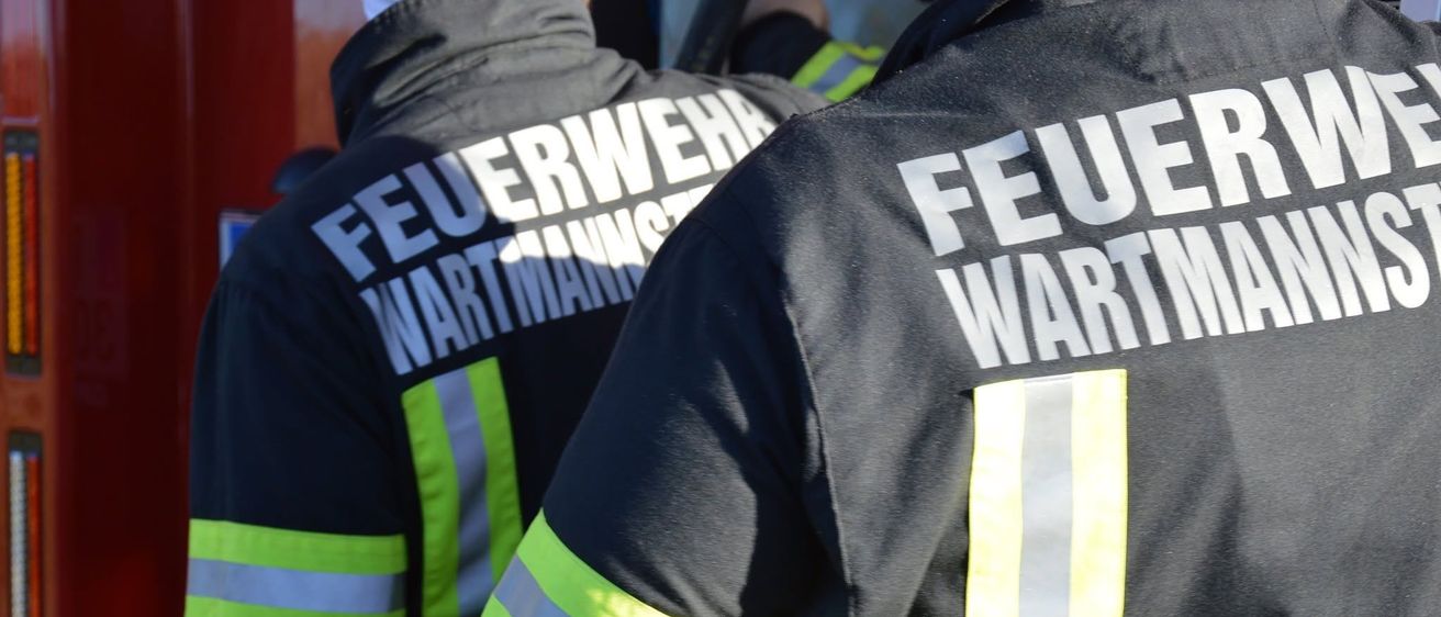 Zwei Feuerwehrleute in reflektierenden Uniformen, einer mit 'Feuerwehr' und 'Wartman' auf dem Rücken.