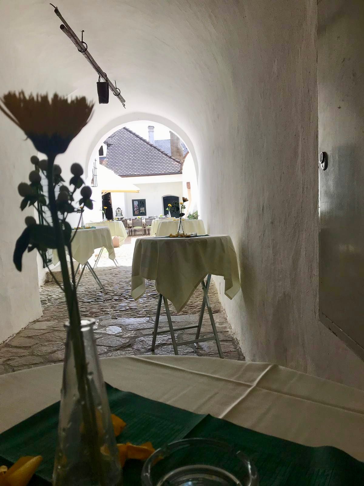 Ein Restaurant mit Tischen, die mit weißen Tüchern bedeckt sind. Die Tische sind von weißen Wänden und einem gepflasterten Weg umgeben.