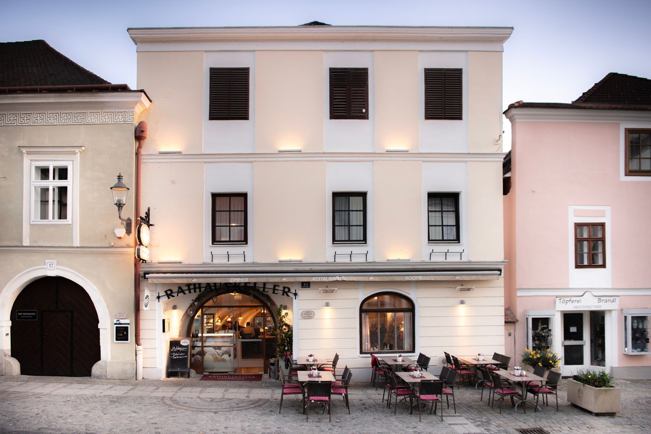 Die Vorderseite eines Restaurants mit Sitzgelegenheiten im Freien und einem Menübrett über dem Eingang. Das Gebäude hat mehrere Fenster und einen Balkon.