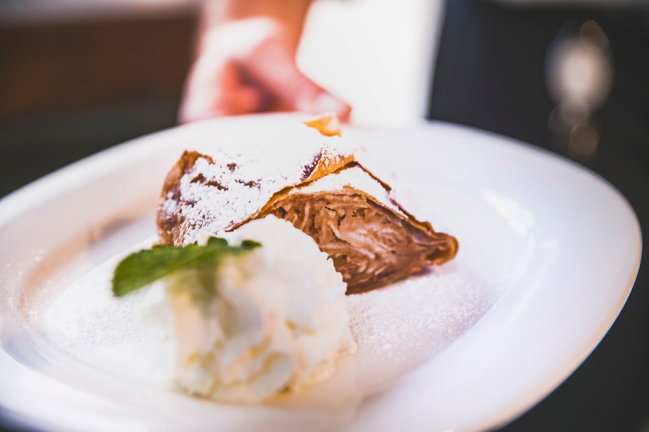 Ein Dessert auf einem weißen Teller, mit Puderzucker bestreut, begleitet von einer Kugel Eiscreme und einem Minzblatt.
