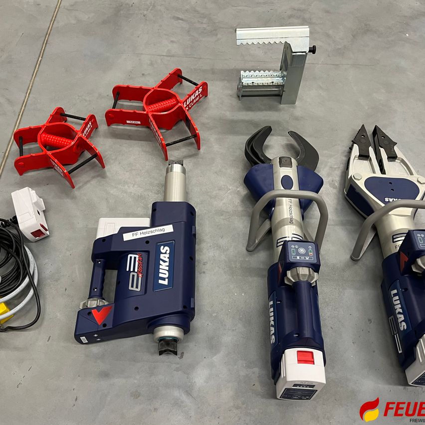 Mehrere mechanische Werkzeuge, darunter zwei große blaue und silberne sowie zwei kleinere rote und ein silbernes Werkzeug mit Zähnen, sind auf einem Betonboden angeordnet.