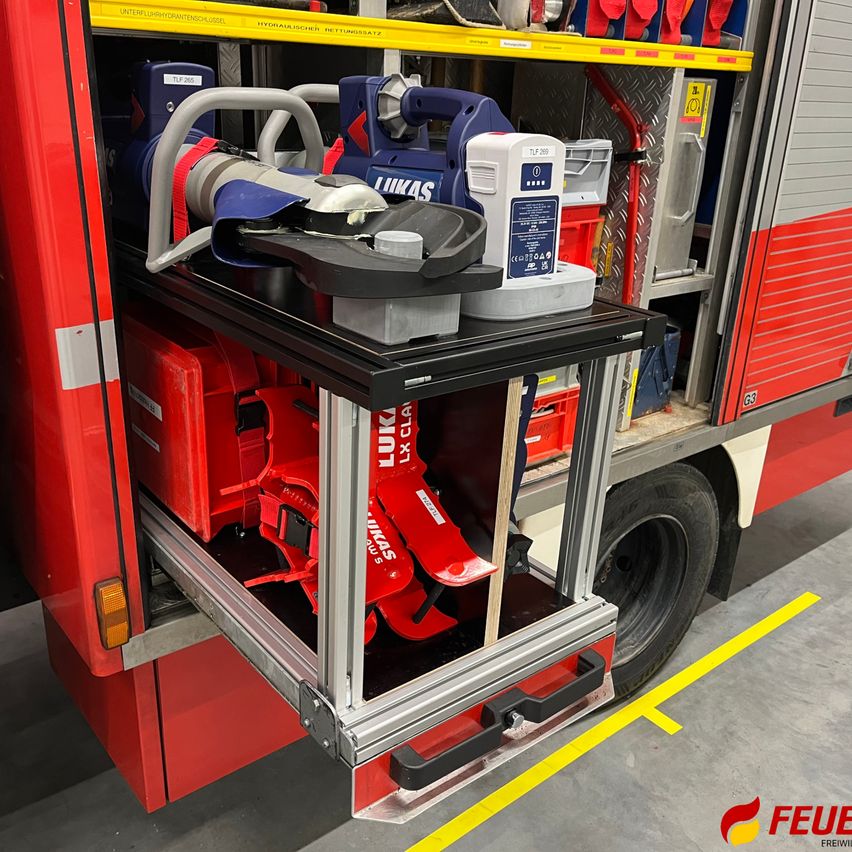 Der Laderaum eines Feuerwehrwagens ist geöffnet und zeigt verschiedene Feuerwehrgeräte. Die Ausrüstung umfasst ein rotes Likas-Gerät, ein blaues Likas-Gerät und ein weißes und blaues Gerät auf einem Regal.