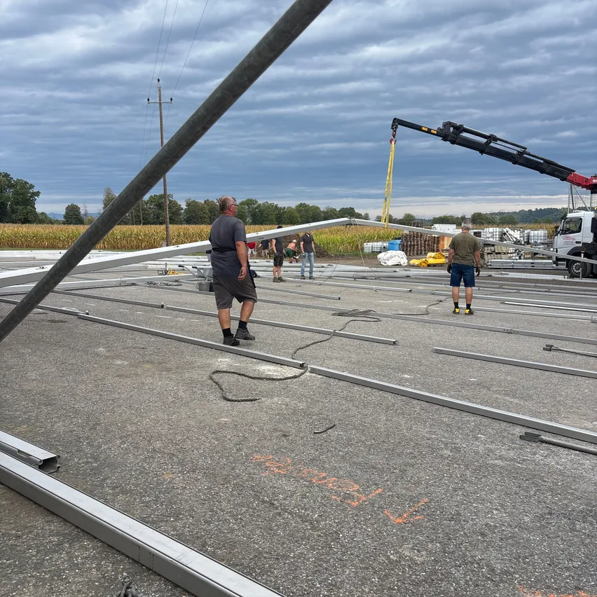 Eine Gruppe von Arbeitern installiert Metallbalken auf einer Baustelle unter einem bewölkten Himmel.