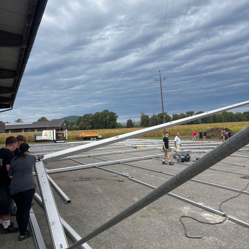 A group of people are working on a large metal structure in an open field under a cloudy sky.