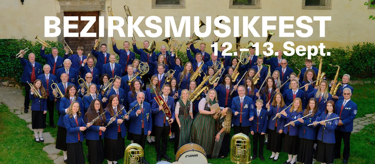 A music band in blue uniforms poses for a photo outside a building with white text that reads 'RKS MUSIK' and the date '12.1-13'. They hold various instruments like trumpets, trombones, and drums.