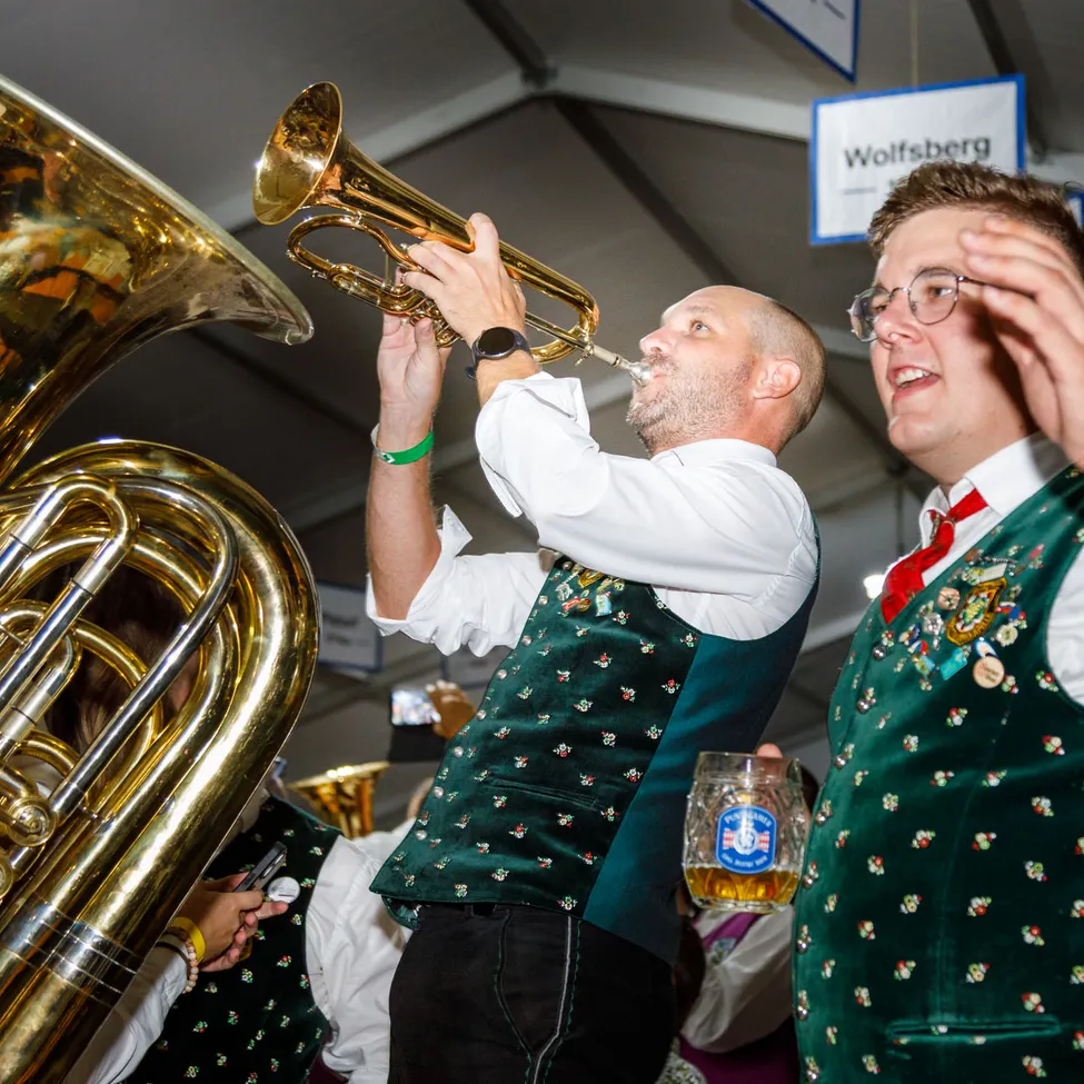 Ein Mann spielt Tuba, während ein anderer Mann ein Bierglas hält.