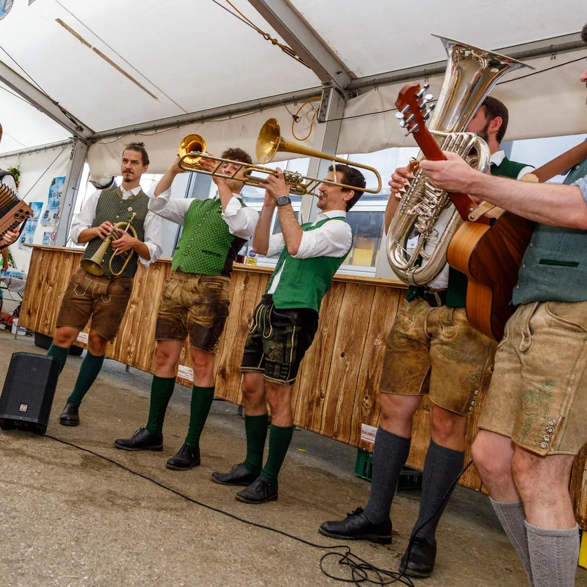 Fünf Männer in traditioneller deutscher Kleidung spielen auf der Bühne mit verschiedenen Musikinstrumenten.