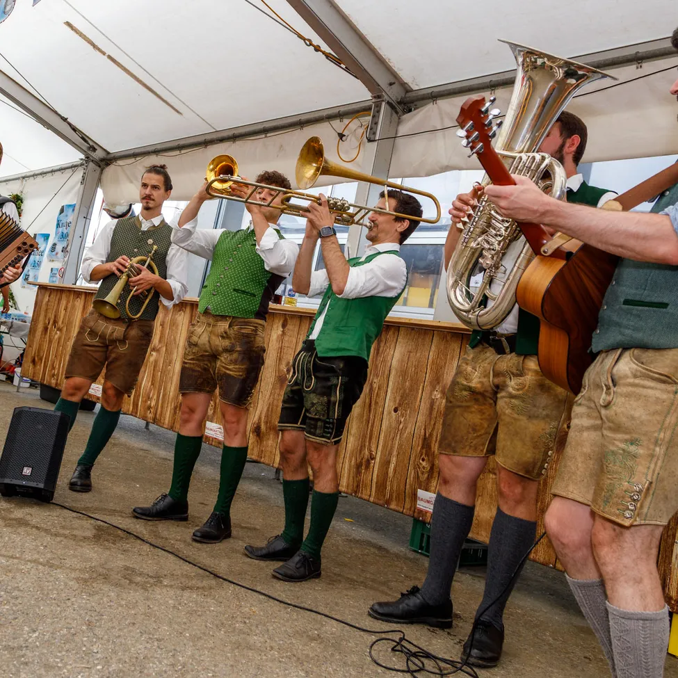Fünf Männer in traditioneller deutscher Kleidung spielen auf der Bühne mit verschiedenen Musikinstrumenten.