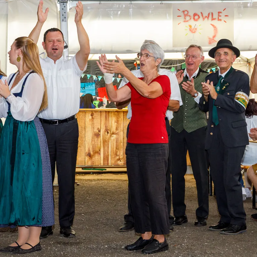 Eine Gruppe von Menschen steht zusammen und klatscht. Sie sind in traditioneller Kleidung gekleidet.