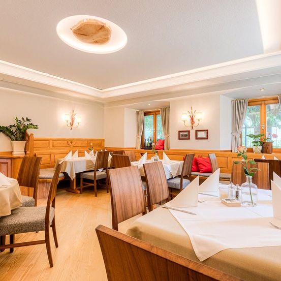 Ein gut eingerichteter Essbereich mit Holztischen, Stühlen und einer warmen Atmosphäre. Der Raum hat weiße Wände, Holzböden und eine Decke mit einem Holzdesign.
