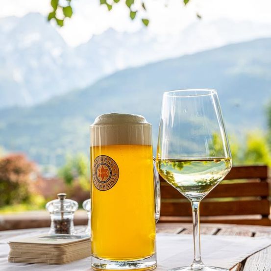 Ein Glas Bier und ein Weinglas auf einem Tisch mit Bergblick.