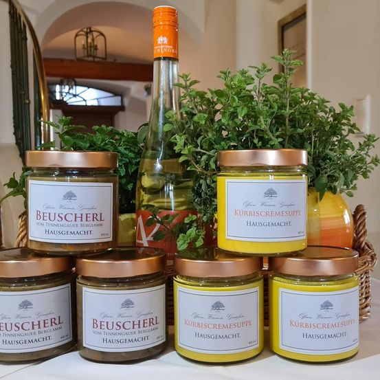 Eine Sammlung von Gläsern mit Kupferdeckeln, darunter eines mit dem Etikett 'BeuscherL', und eine Flasche mit orangefarbenem Verschluss, alles auf einem Tisch angeordnet, mit einer Pflanze im Hintergrund.