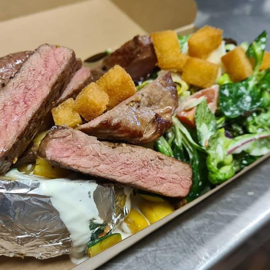 Ein Nahaufnahme von einem Gericht mit Steak, Salat und Croutons in einer Pappschachtel. Das Steak ist saftig und gut gegart.