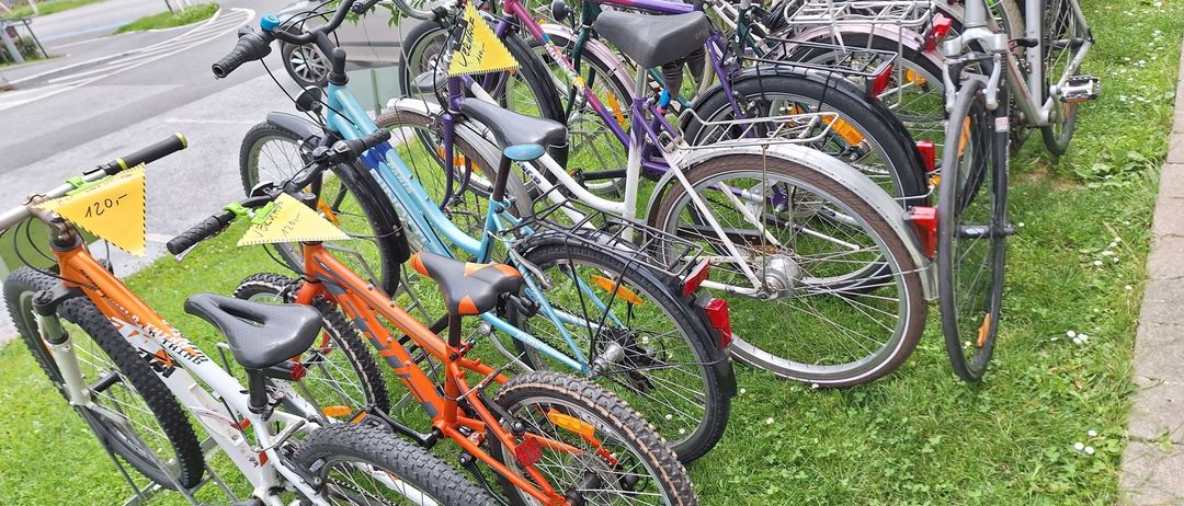 Eine Reihe von Fahrrädern in verschiedenen Farben ist auf dem Rasen in der Nähe einer Straße mit einem Busch und einem Schild im Hintergrund geparkt.