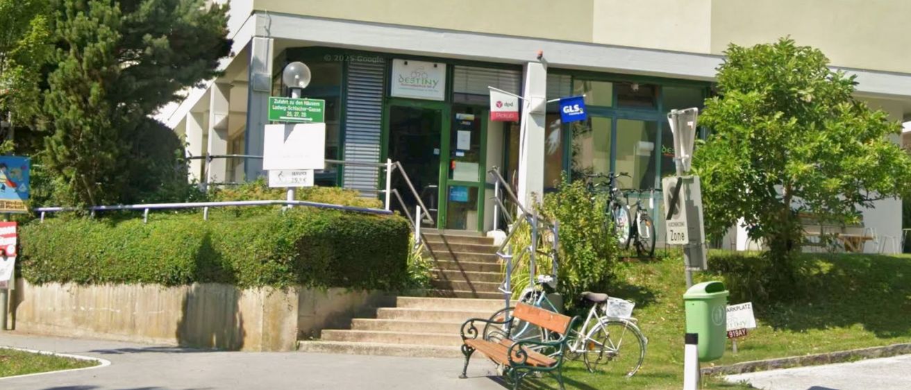 Ein Gebäude mit einem Schild 'No Destiny' über dem Eingang. Stufen, die zum Eingang führen. Geparkte Fahrräder an der Seite. Eine Bank mit einem Mülleimer in der Nähe.