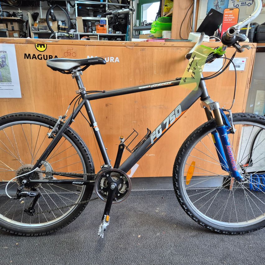 Ein schwarzes Mountainbike mit blauen Akzenten und der Aufschrift 'FG 750' am Rahmen steht in einem Geschäft.