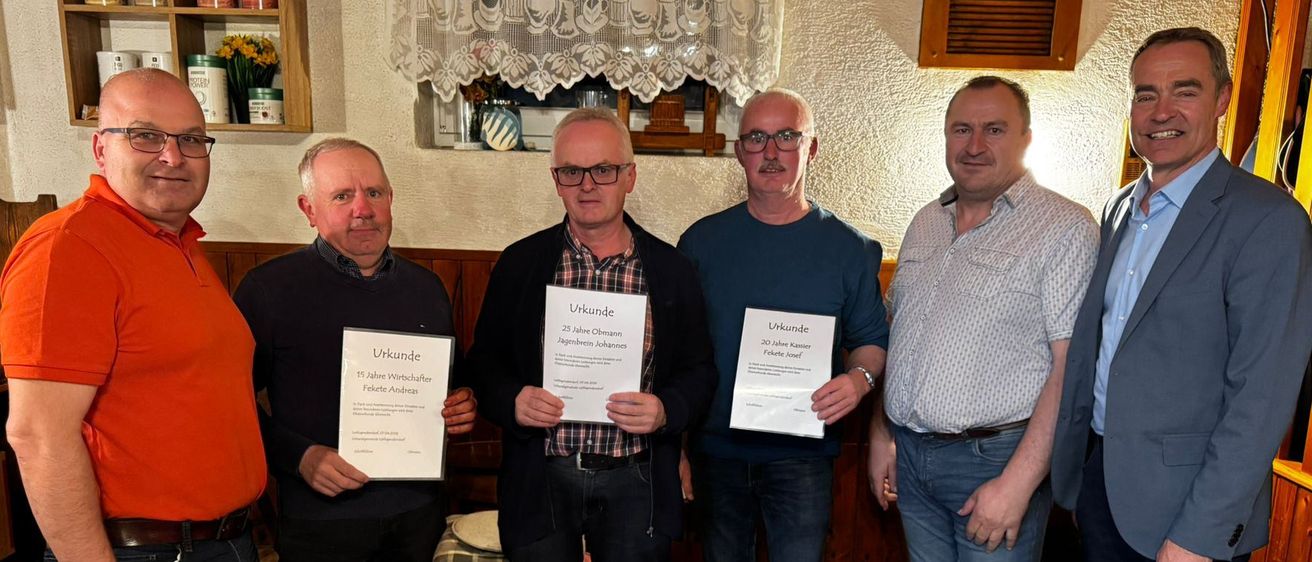Fünf Männer stehen in Innenräumen und halten Urkunden in der Hand. Sie tragen alle eine Brille, Schuhe und Gürtel. Der Raum ist mit einem Vorhang, einem Regal und anderen Gegenständen dekoriert.