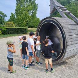 Kinder spielen auf einer großen Holzspielplatzstruktur in einem Außenbereich.