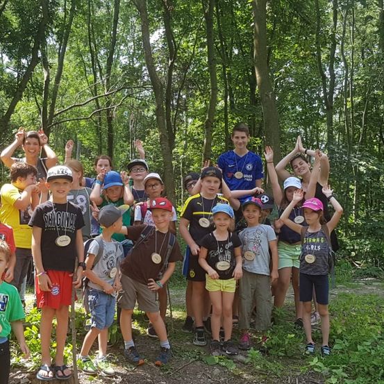 Eine Gruppe von Kindern und Erwachsenen im Wald, einige mit Medaillen, posieren für ein Foto.