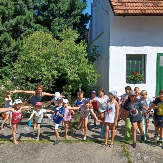 Eine Gruppe von Kindern und Erwachsenen posiert für ein Foto vor einem weißen Gebäude mit grünen Fenstern und einem roten Dach.