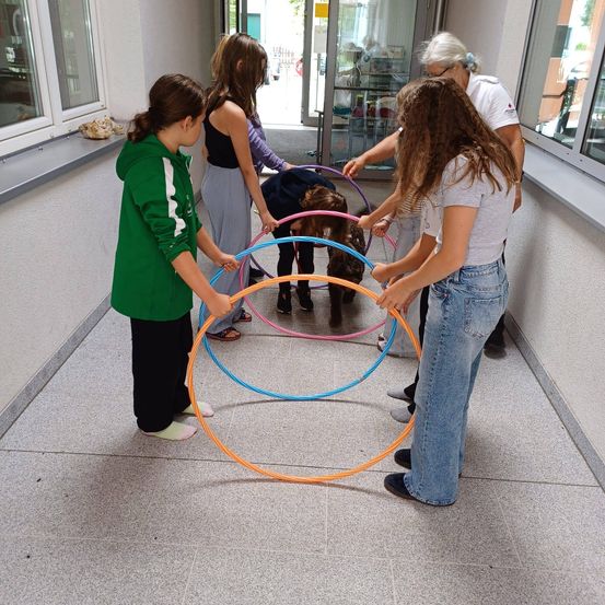 Eine Gruppe junger Mädchen spielt mit Hula-Hoops in einem Flur, wobei zwei von ihnen auf dem Boden knien.