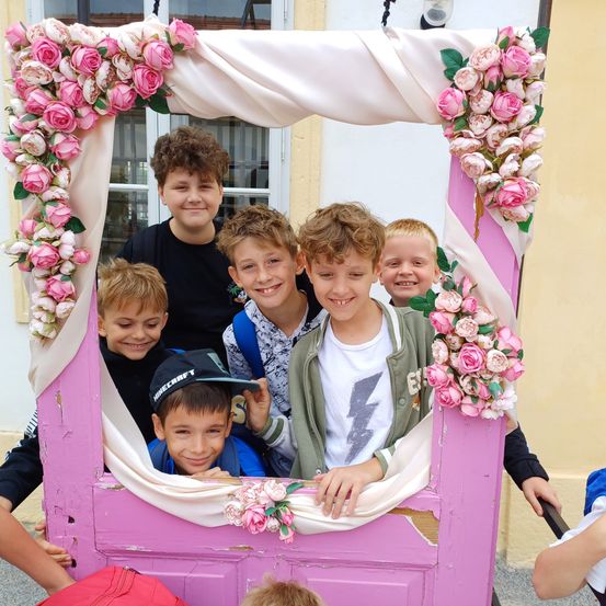 Eine Gruppe junger Jungen posiert in einem dekorierten rosa Rahmen mit rosa Blumen, lächelt und schaut zur Kamera.