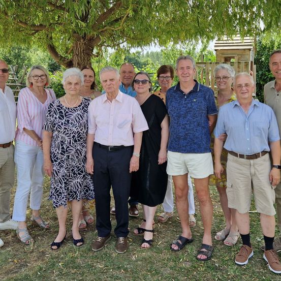 Eine Gruppe von Menschen, einschließlich Männer und Frauen, stehen zusammen in einem Garten, lächeln und posieren für ein Foto.