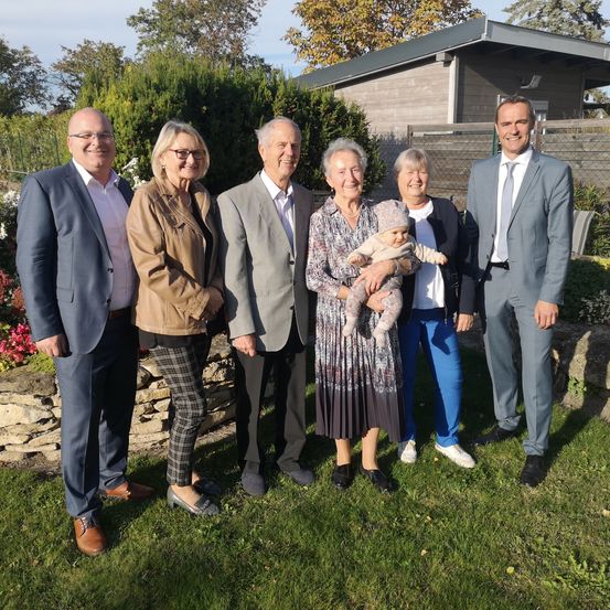 Eine sechsköpfige Familie steht vor einem Haus mit Garten auf dem Rasen und lächelt für ein Foto.