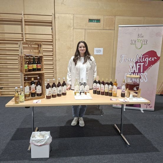 Eine Frau steht hinter einem Tisch mit Flaschen Fruchtsaft, einem Schild für Bio Quest und einem Mülleimer.