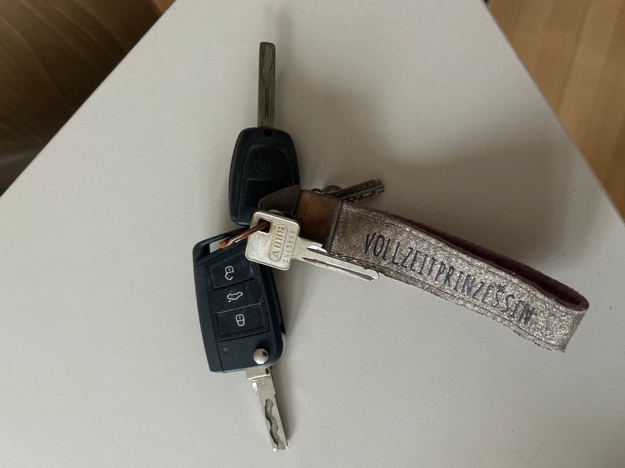 A silver keychain and two keys on a white surface. The keychain has text and a metallic finish. One key has a lock symbol, while the other has a key symbol.