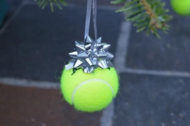 Ein Tennisball-Anhänger mit einer silbernen Schleife, der an einem Weihnachtsbaum hängt.