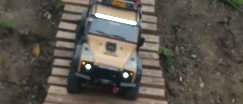 Eine Holzrampe führt von einem kleinen Hügel hinab. Ein Spielzeug-Jeep mit Frachtablage fährt darauf herunter.