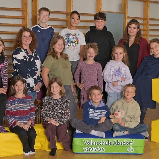 Eine Gruppe von Schülern und Lehrern posiert für ein Foto in einem Klassenzimmer mit einem gelben und grünen Hintergrund, der Volksschule Absdor 2025/26 4b sagt.