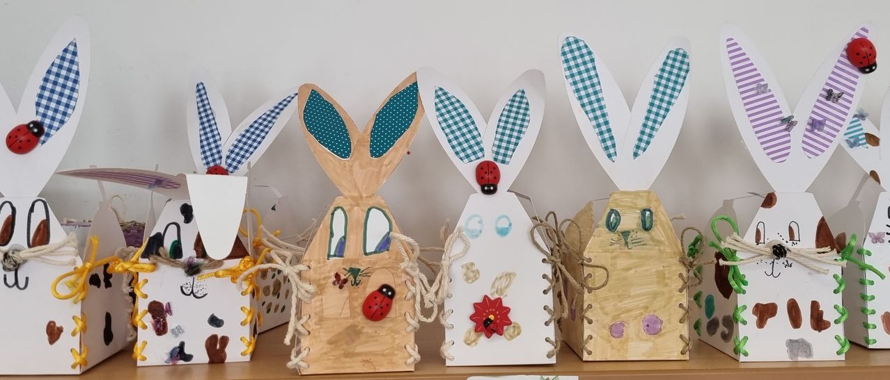 Fünf handgefertigte Kaninchen-förmige Boxen mit verschiedenen Dekorationen werden auf einer Holzoberfläche ausgestellt. Jede Box hat einzigartige Merkmale, einschließlich Marienkäfer und Blumen. Sie sind zum Halten von Gegenständen konzipiert und scheinen handgemacht zu sein.