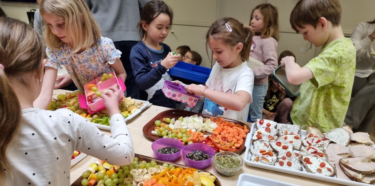 Eine Gruppe junger Mädchen bereitet sich darauf vor, verschiedene Obst- und Gemüsesorten auf einem Tisch zu essen, einige in pinkfarbenen Lunchboxen.