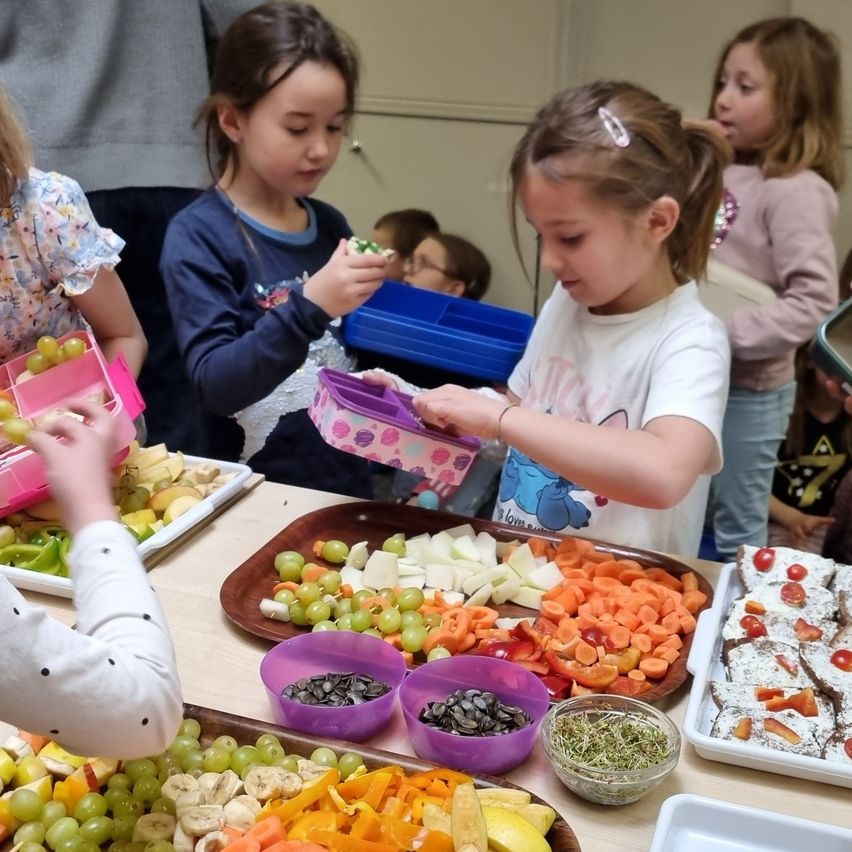 Eine Gruppe junger Mädchen bereitet sich darauf vor, verschiedene Obst- und Gemüsesorten auf einem Tisch zu essen, einige in pinkfarbenen Lunchboxen.