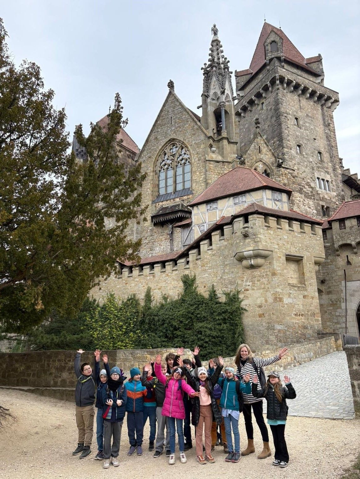 Eine Gruppe von Kindern und Erwachsenen posiert für ein Foto vor einer großen Burg. Sie alle lächeln und winken.