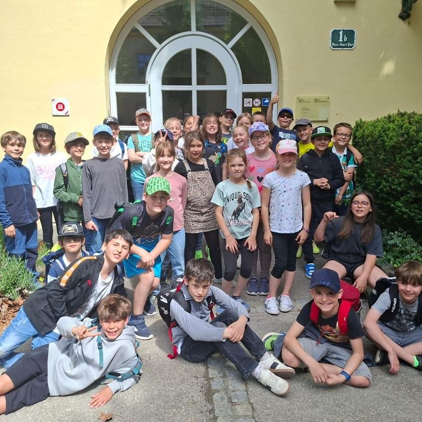 Eine Gruppe junger Schüler, einige mit Hüten und Brillen, posiert für ein Foto vor einem Gebäude.