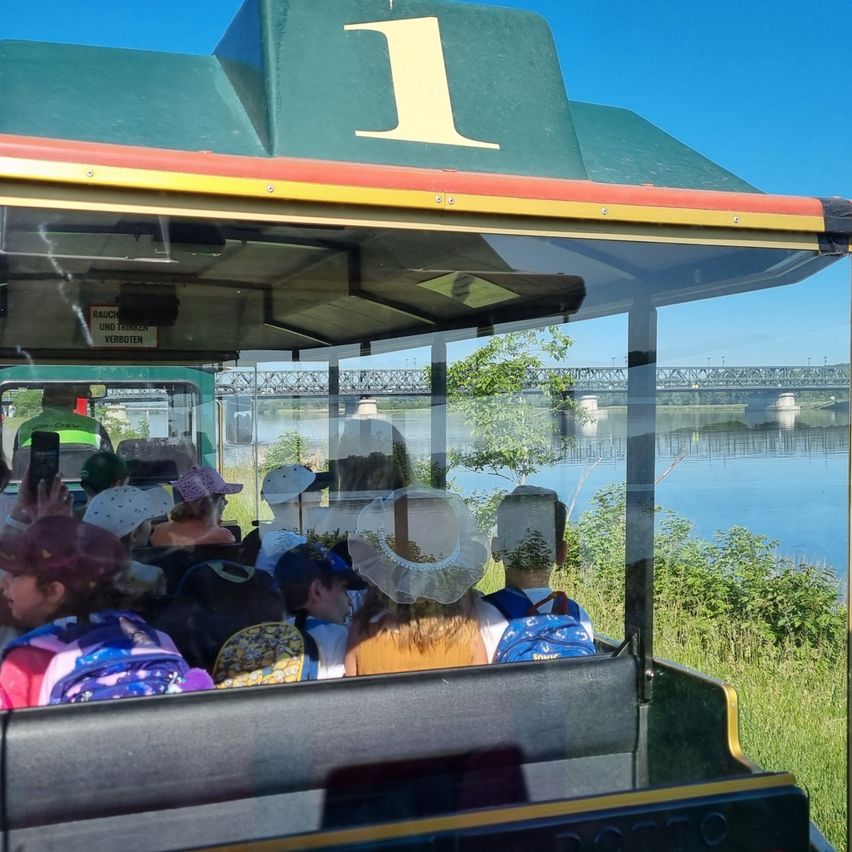 Touristenfahrt mit Passagieren, zeigt einen Fluss und eine Brücke im Hintergrund. Die Fahrt ist mit der Nummer eins beschriftet.