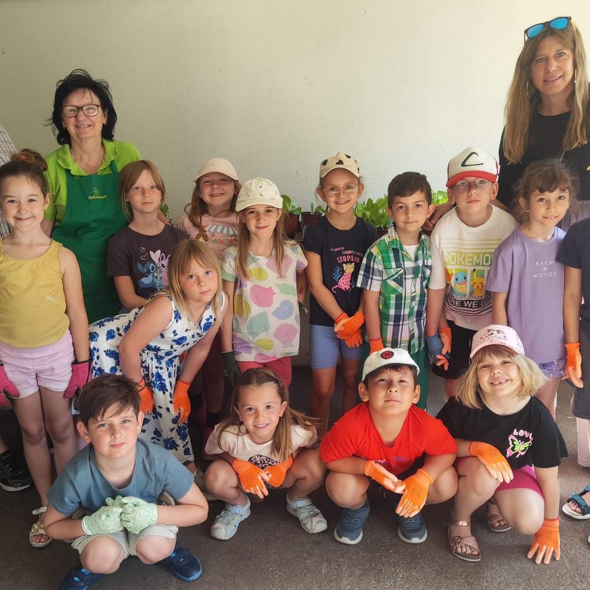 Eine Gruppe von Kindern und Erwachsenen mit Handschuhen und Mützen, die lächelnd für ein Foto im Garten posieren.