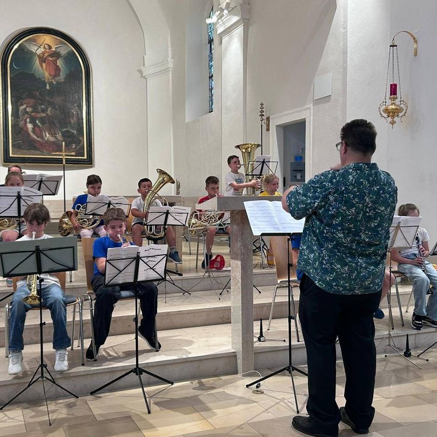 Ein Bandproben in einer Kirche, Kinder spielen Instrumente, ein Dirigent steht davor.